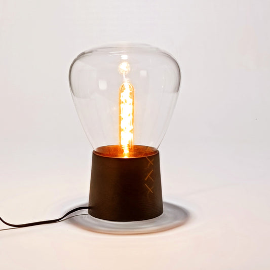 Candeeiro de mesa em vidro soprado com base de madeira, design simples e luz quente.