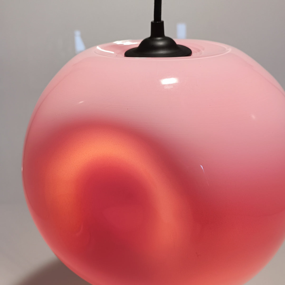 Close-upweergave van de hanglamp van koraalroze glas, met zwart snoer en plafondroos