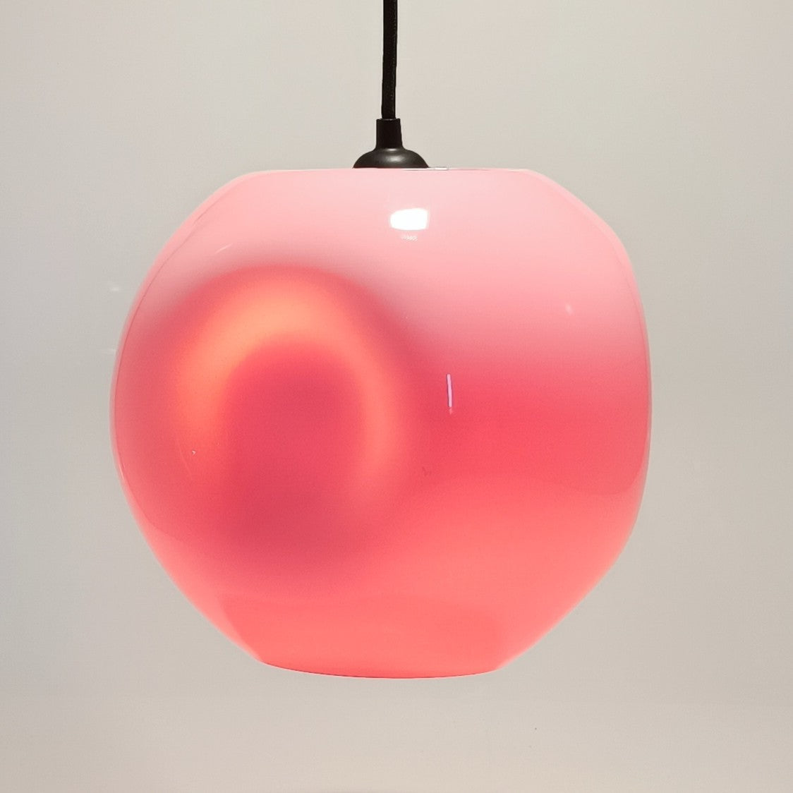 Verlichte hanglamp van koraalroze glas, met de kleurtint van het stuk in de verf