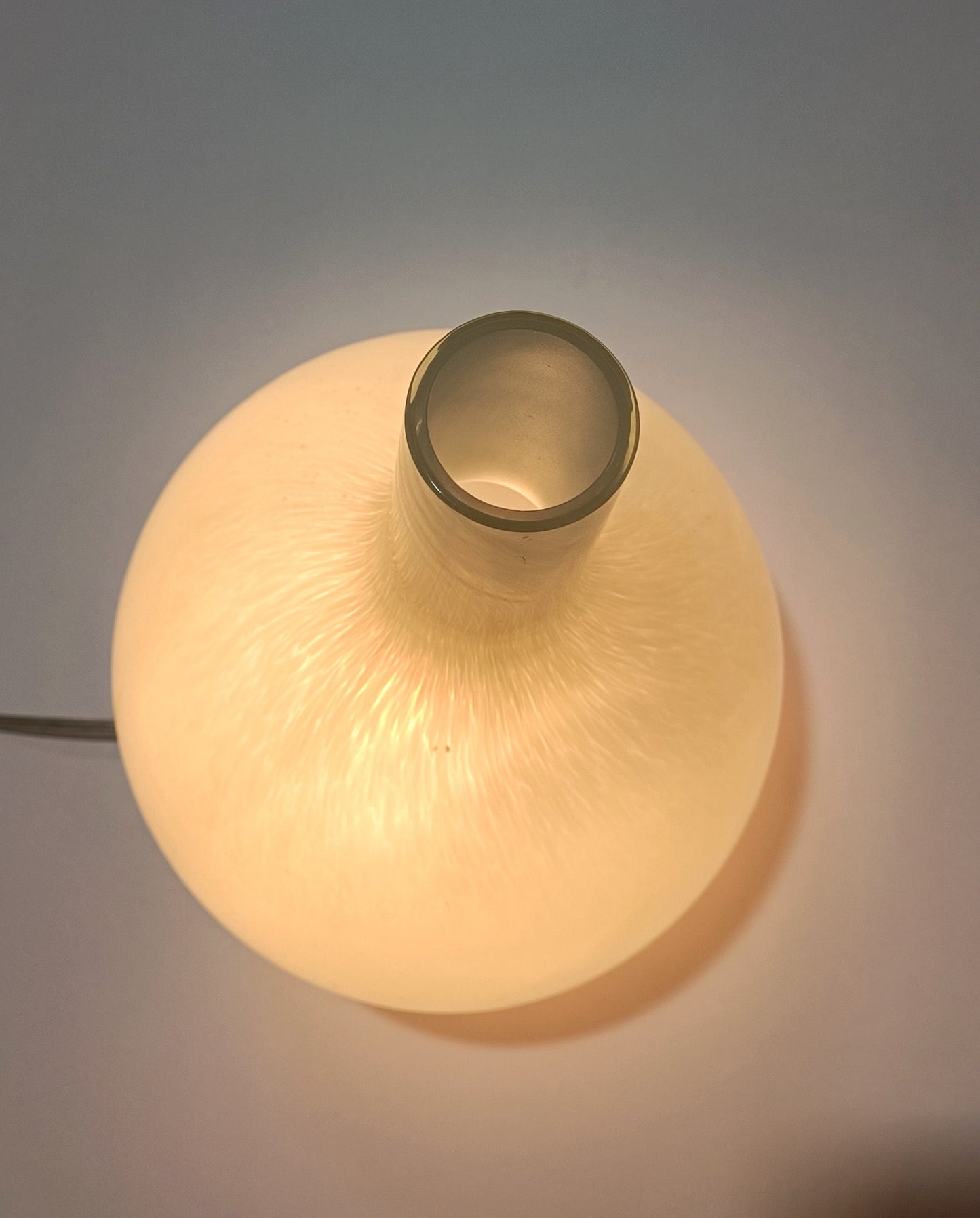 Candeeiro Halo Brando visto de trás, em vidro branco opaco e formato arredondado.