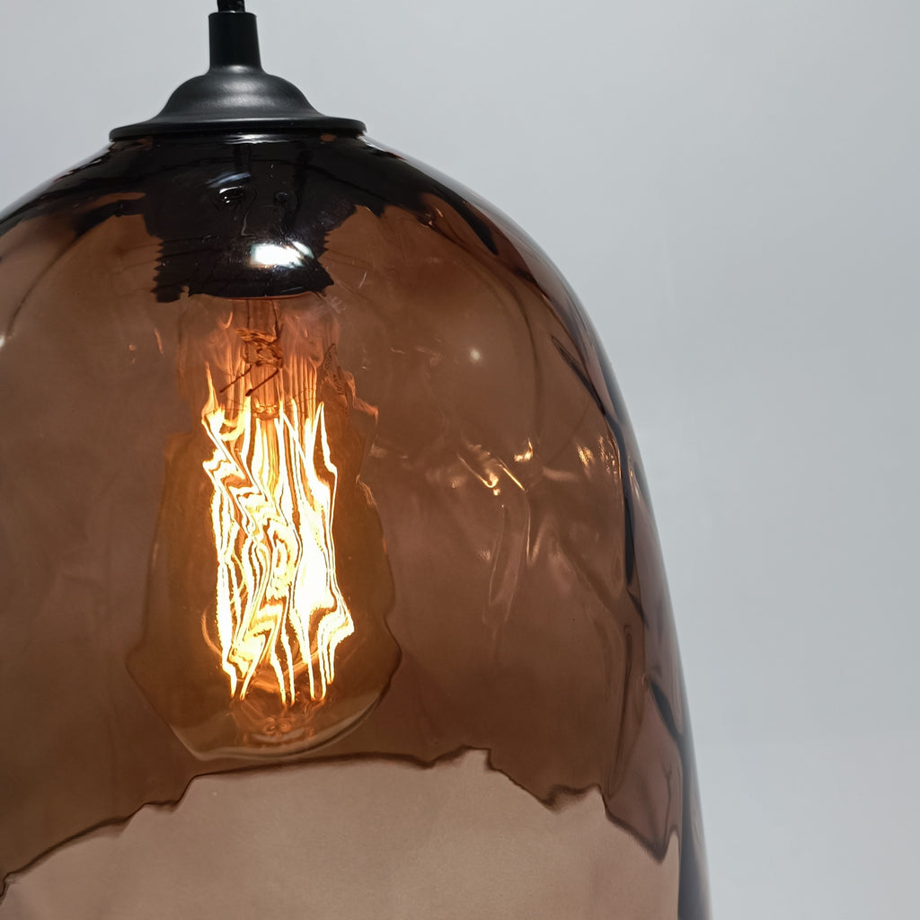 Lámpara colgante DÔMEA encendida, con el brillo ámbar del filamento atravesando el vidrio soplado