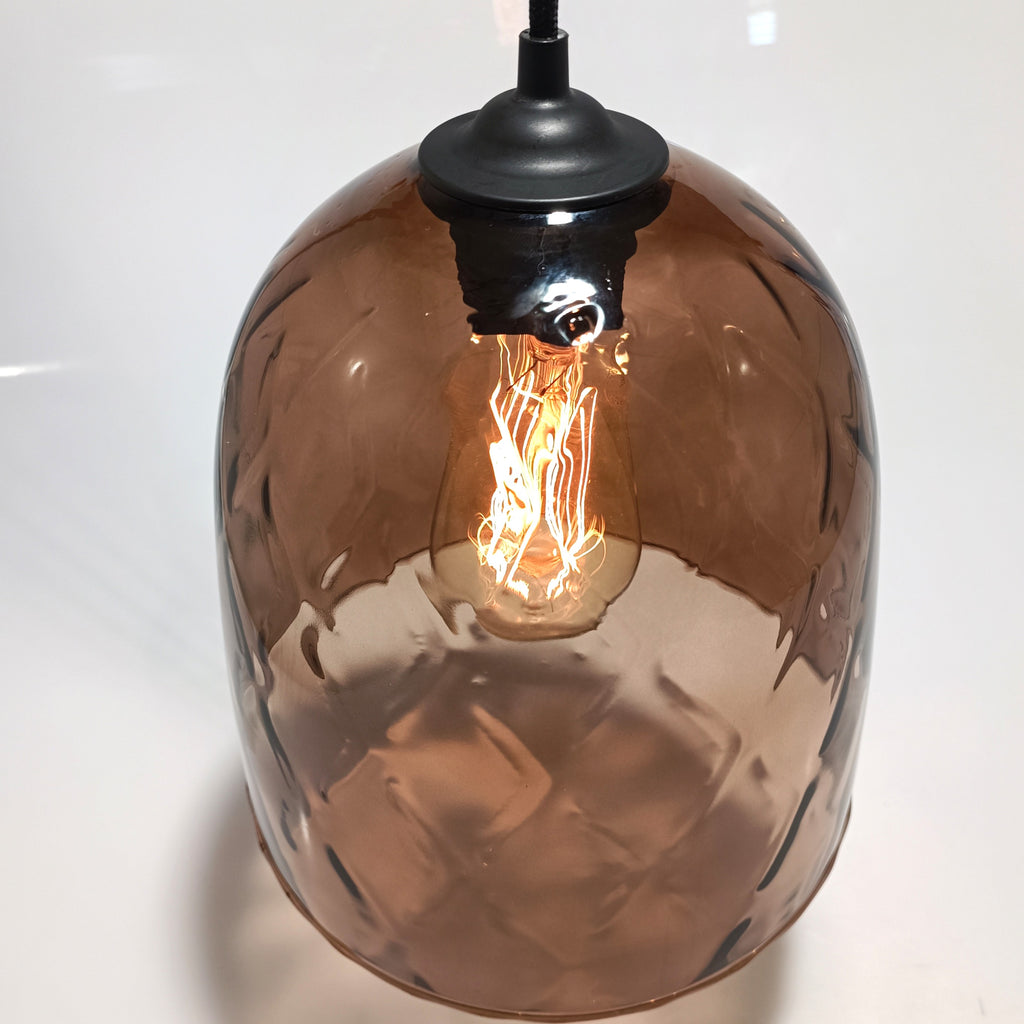 Detalle de la cúpula de vidrio soplado translúcido de la lámpara DÔMEA con bombilla de filamento encendida