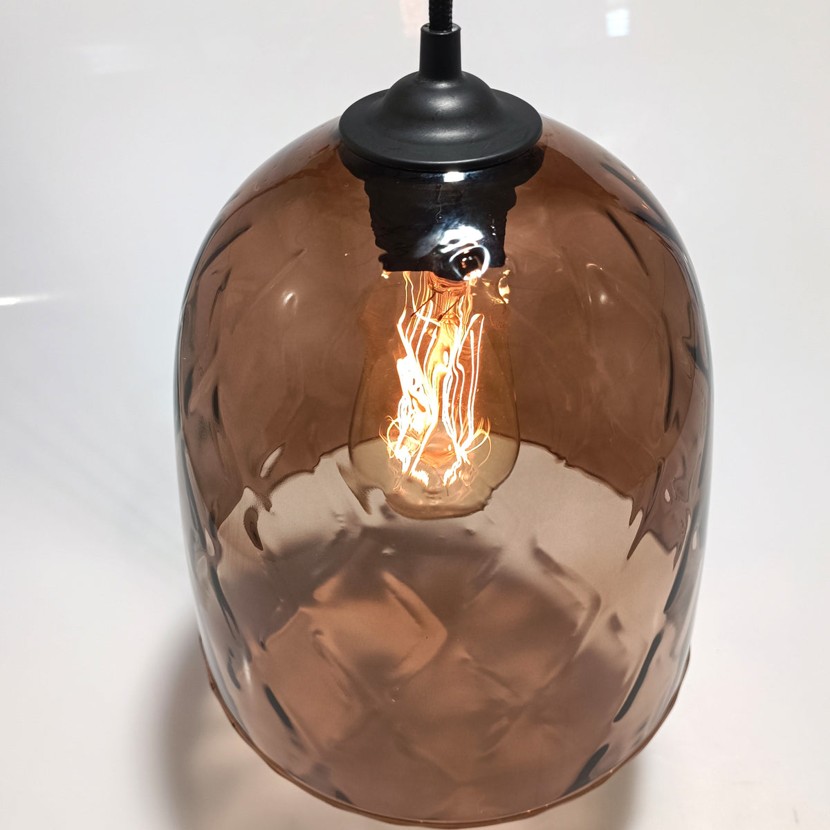 Close-up of the DÔMEA pendant's translucent blown glass dome with a lit filament bulb