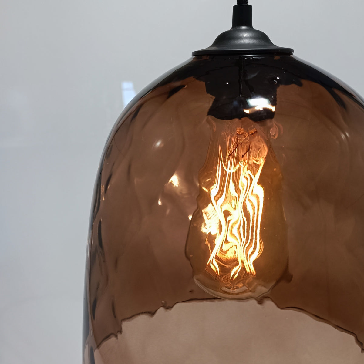 Warm filament light glowing through the wine-brown glass of the DÔMEA pendant