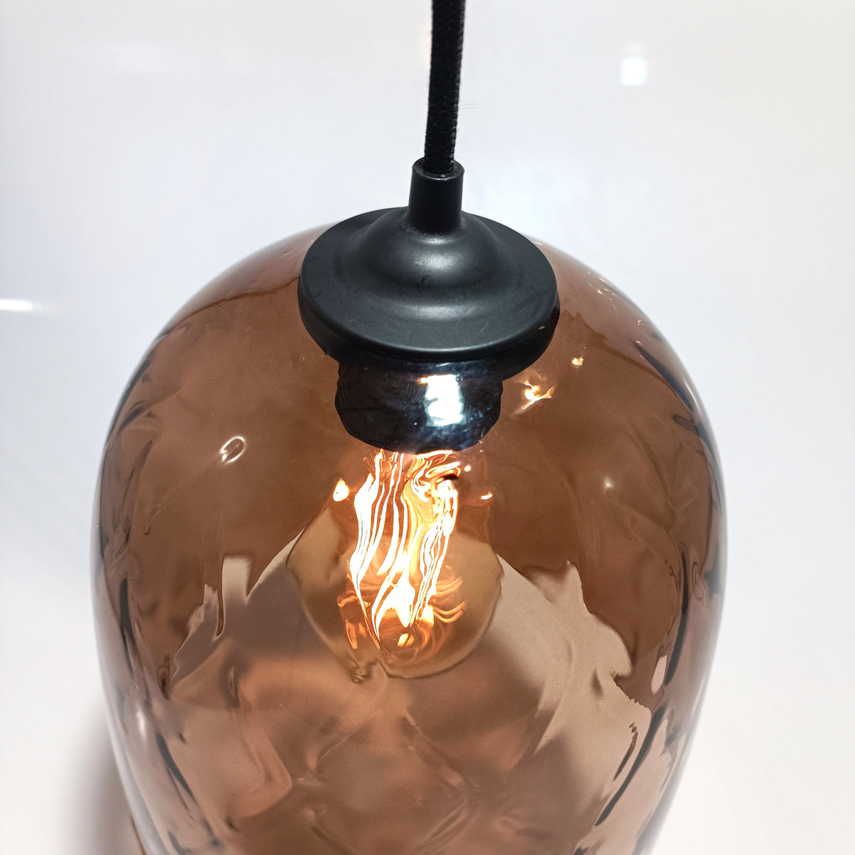 Close-up of the DÔMEA pendant top: matte black lamp holder and metal finish over the wine-brown glass